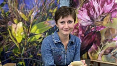 Maggie Jeffries – image of a women sitting in front of a floral wall