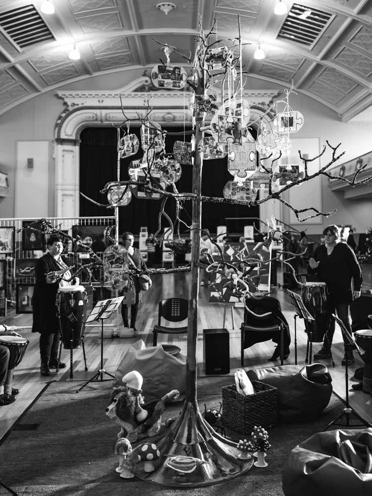 A black and white image of a tree and people standing around the tree drumming by Langford Support Services